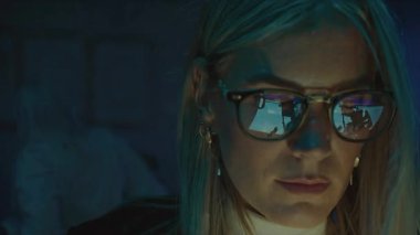 A focused professional working in a stylish workspace, showcasing reflective glasses and ambient lighting.