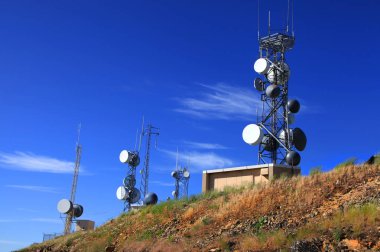 Tall communication towers against blue sky clipart
