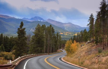 Colorado 'nun dolambaçlı yolunun yanındaki kozalaklı ağaçlar bulutlu gökyüzü ile kayalık dağlar.