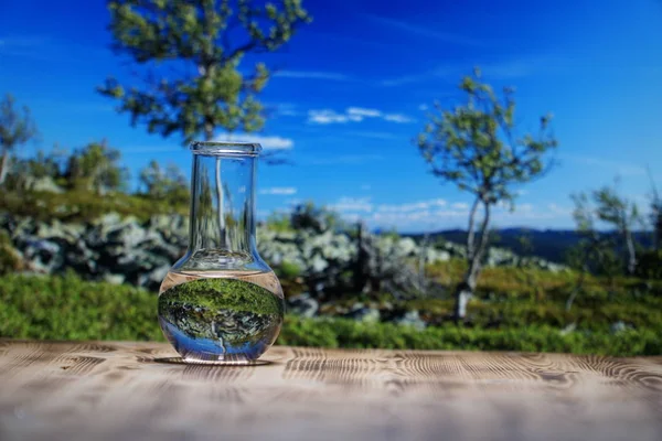 Rent vatten i ett glas laboratorium kolv på träbord på berget bakgrund. Ekologiska begrepp, test av renhet och vattenkvalitet. — Stockfoto