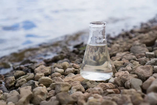 Chemiekolben mit Wasser, See oder Fluss im Hintergrund. — Stockfoto