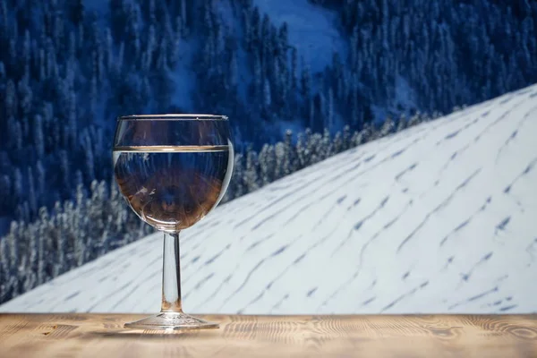 Ett glas rent vatten står på ett träbord mot berget vinterlandskapet. — Stockfoto