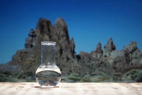 Água limpa em um frasco de laboratório de vidro em mesa de madeira no fundo da montanha. Conceito ecológico, o teste de pureza e qualidade da água . — Fotografia de Stock