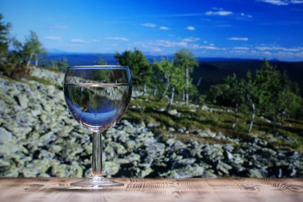 Ett glas glas glas med rent vatten står på ett träbord mot ett bergslandskap. — Stockfoto