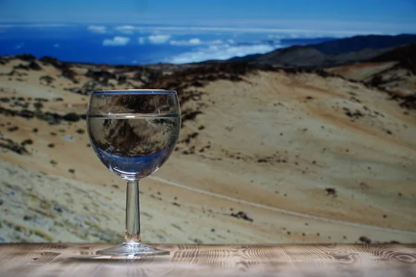 一张有清水的玻璃玻璃杯, 站在木桌上, 反对山上的风景。. — 图库照片