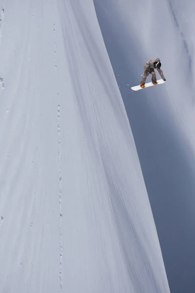 Snowboardos repül a háttérben a havas lejtőn. Extrém téli sportok, snowboardozás. — Stock Fotó
