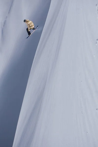 Snowboarder voando no fundo da encosta nevada. Esportes de inverno extremos, snowboard. — Fotografia de Stock