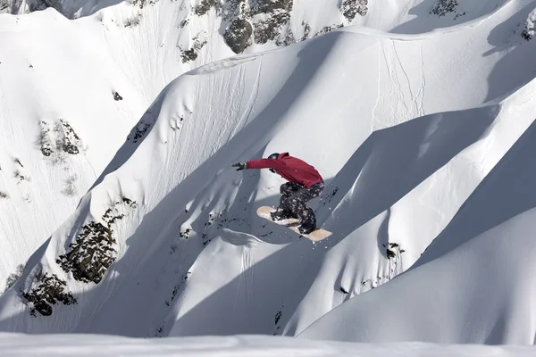 Snowboarder volant sur le fond d'une pente enneigée. Sports d'hiver extrêmes, snowboard. — Photo