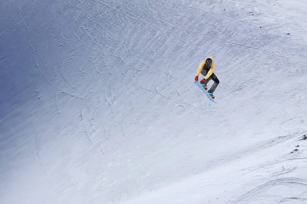 Snowboardista letící na pozadí zasněženého svahu. Extrémní zimní sporty, snowboarding. — Stock fotografie