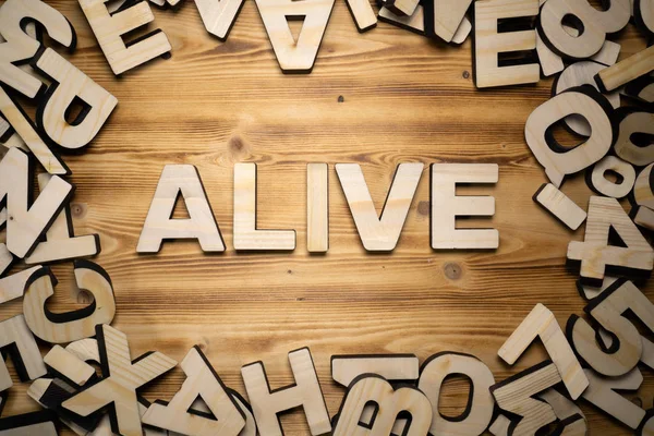 Kata ALIVE dibuat dengan huruf blok tergeletak di papan kayu — Stok Foto