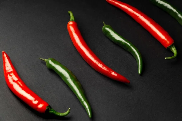 Πράσινες και κόκκινες πιπεριές τσίλι σε μαύρο φόντο. Καυτά πικάντικα τρόφιμα. — Φωτογραφία Αρχείου