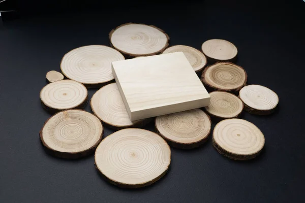 Pine tree cross-sections with annual rings and wooden square on black surface. Lumber piece close-up, top view.