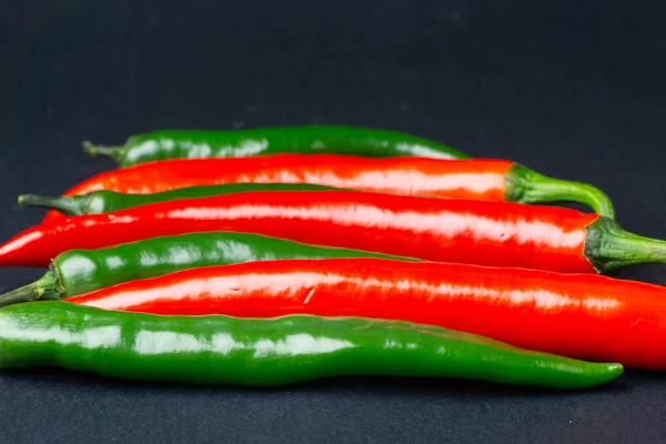 Πράσινες και κόκκινες πιπεριές τσίλι σε μαύρο φόντο. Καυτά πικάντικα τρόφιμα. — Φωτογραφία Αρχείου