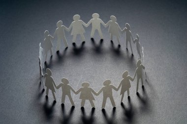 Circle of paper people holding hands on dark surface. Community, union concept. Society and support. clipart