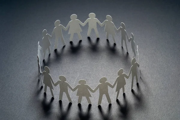 Circle of paper people holding hands on dark surface. Community, union concept. Society and support.