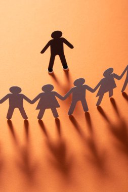 Kağıt insan figürü ayakta kırmızı yüzey üzerinde el ele tutuşarak kağıt insanların önünde. Bulling, segregasyon, çatışma kavramı.