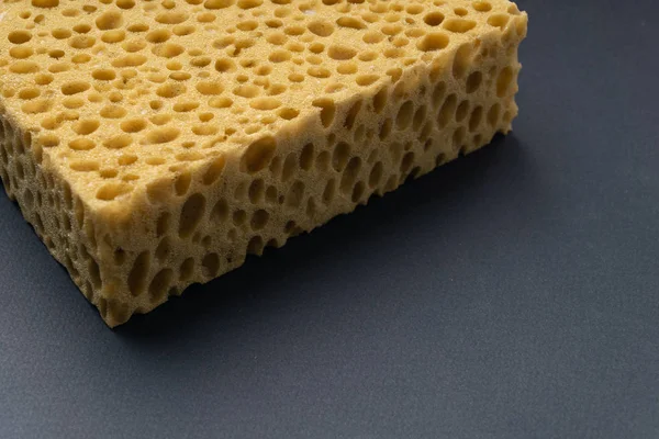 Close up view of cleaning sponge, mesh structure pattern on black surface. Yellow sponge close-up. — Stock Photo, Image