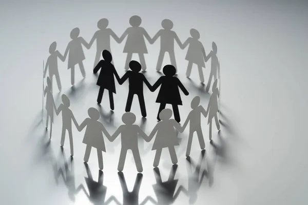 Tres figuras de papel humano rodeadas por un círculo de personas de papel cogidas de la mano en la superficie blanca. Bulling, segregación, concepto de conflicto . — Foto de Stock