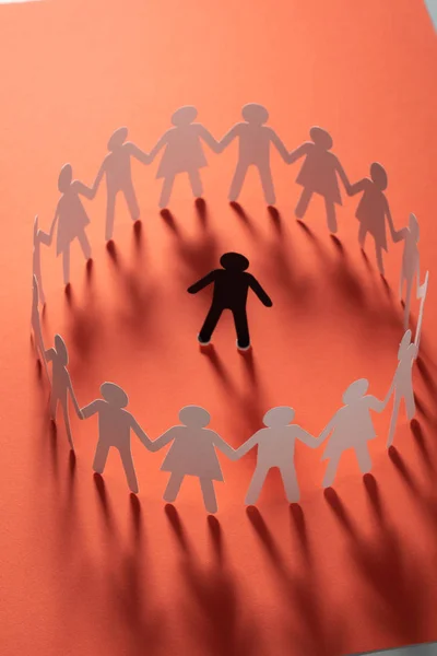 Бумажная человеческая фигура, окруженная кругом бумажных людей, держащихся за руки на красной поверхности. Буллинг, сейв, концепция конфликта . — стоковое фото