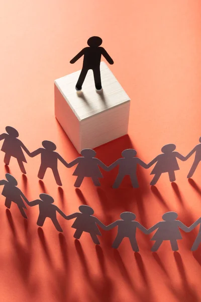 Figura líder de papel delante de gente de papel tomados de las manos en la superficie roja. Líder, político, jefe . —  Fotos de Stock