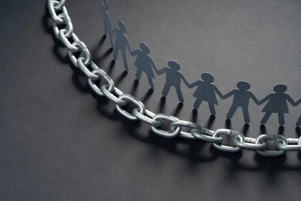 Figuras de papel humano paradas frente a una cadena metálica sobre una superficie negra. Libertad, derechos humanos, independencia . — Foto de Stock