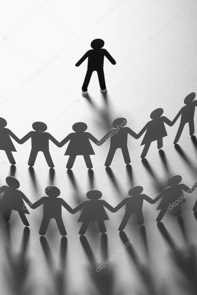 Paper human figure standing in front of paper people holding hands on white surface. Bulling, segregation, conflict concept.