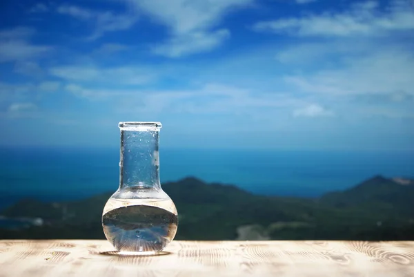 Clean water in a glass laboratory flask on wooden table on sea background. Ecological concept, the protection of water resources, the test of purity and quality of water.