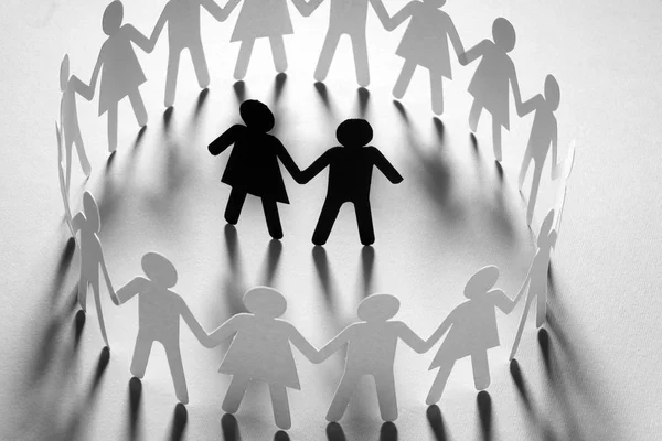Бумажная фигура пары, окруженная кругом бумажных людей, держащихся за руки на белой поверхности. Буллинг, меньшинства, концепция конфликта . — стоковое фото