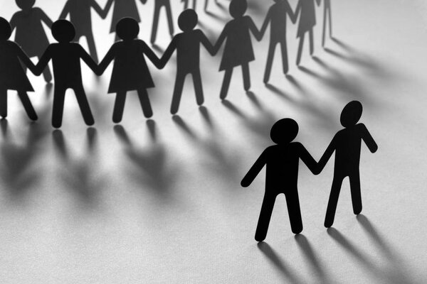 Black paper figure of male couple in front of a crowd of paper people holding hands on orange surface. Social movement, minorities, protest concept.