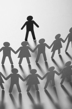 Kağıt insan figürü ayakta beyaz yüzey üzerinde el ele tutuşarak kağıt insanların önünde. Bulling, segregasyon, çatışma kavramı.