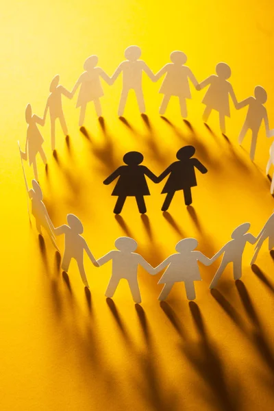 Figurine en papier d'un couple féminin entouré d'un cercle de gens en papier tenant la main sur une surface jaune. Bulling, minorités, concept de conflit . — Photo