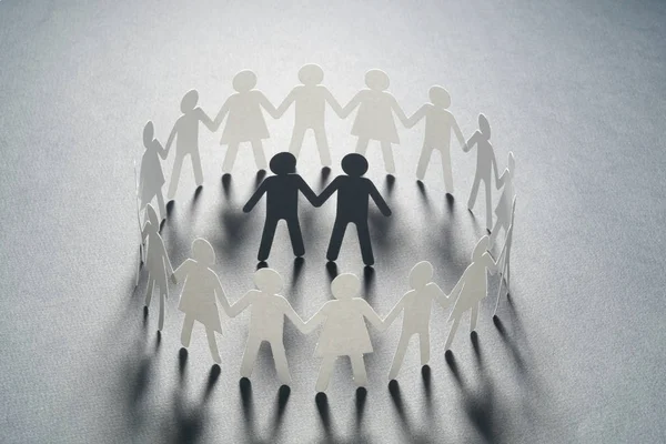 Бумажная фигура мужской пары в окружении круга бумажных людей, держащихся за руки на белой поверхности. Буллинг, меньшинства, концепция конфликта . — стоковое фото