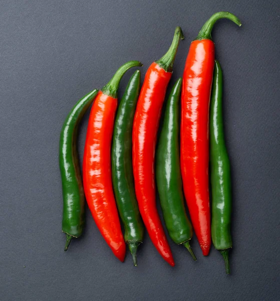 Green and red chili peppers on black background top view. Hot spicy food.