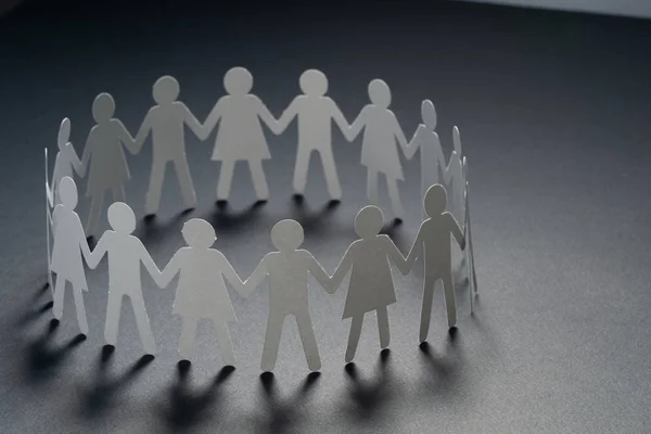 Circle of paper people holding hands on dark surface. Community, union concept. Society and support.