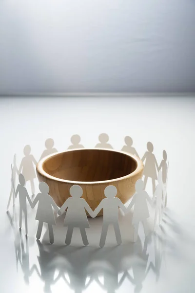 Circle of paper people holding hands in front of big empty bowl. Overpopulation, famine concept.