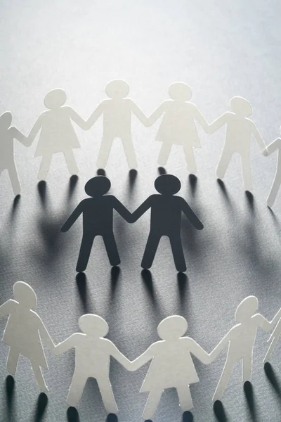 Figura de papel de um casal masculino cercado por círculo de pessoas de papel que mantêm as mãos na superfície branca. Bulling, minorias, conceito de conflito . — Fotografia de Stock