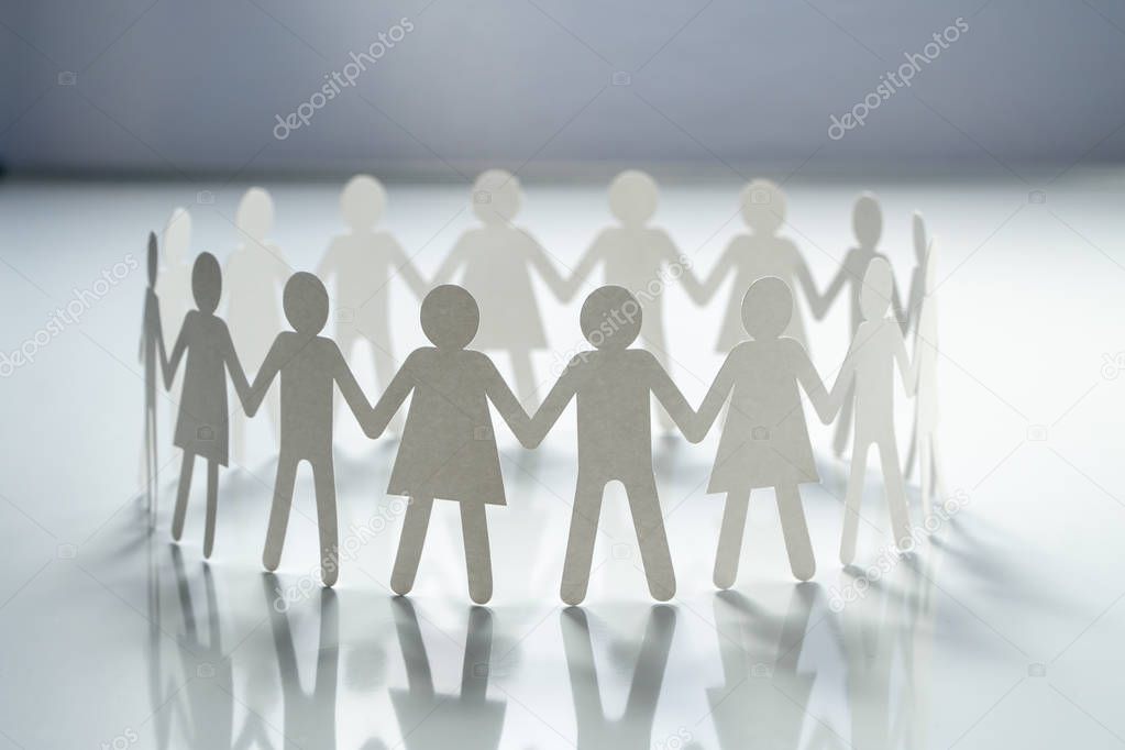 Circle of paper people holding hands on white surface. Community, union concept. Society and support.