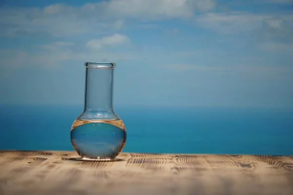 Rent vatten i ett glas laboratorium kolv på träbord på havet bakgrund. Ekologiska begrepp, skydd av vattenresurser, test av renhet och vattenkvalitet. — Stockfoto