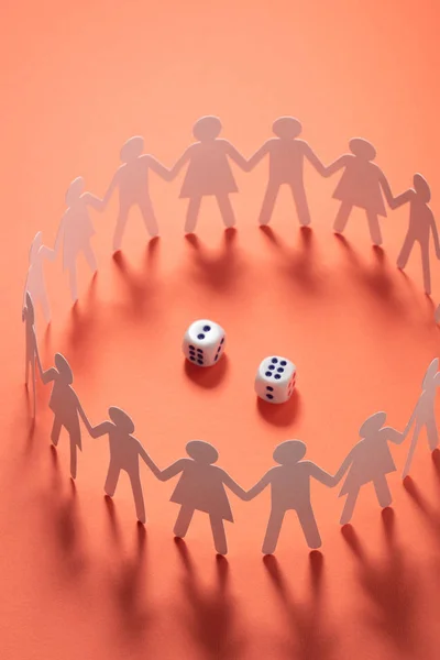 Circle of paper people holding hands in front of two dices. Gambling, addiction concept.