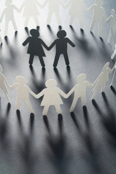 Paper figure of a couple surrounded by circle of paper people holding hands on white surface. Bulling, minorities, conflict concept. — Stock Photo, Image