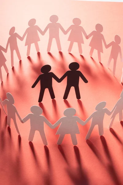 Figura de papel de pareja masculina rodeada por un círculo de personas de papel cogidas de la mano en la superficie blanca. Bulling, minorías, concepto de conflicto . — Foto de Stock