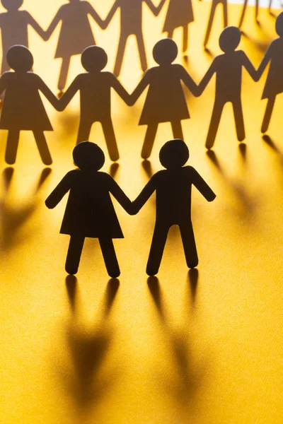 Black paper figure of a couple in front of a crowd of paper people holding hands on yellow surface. Social movement, leadership, protest concept. — Stock Photo, Image
