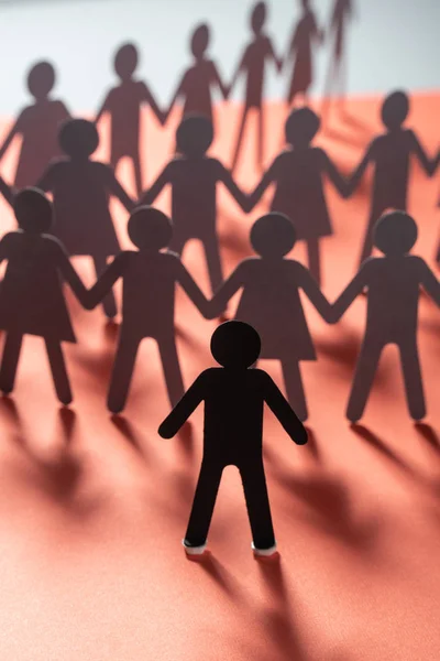 Papel figura humana em pé na frente de pessoas de papel de mãos dadas na superfície vermelha. Bulling, segregação, conceito de conflito . — Fotografia de Stock