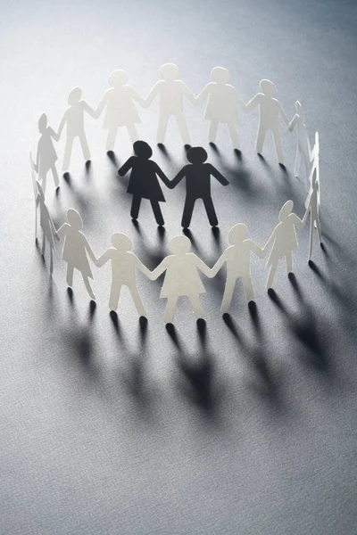 Figura de papel de una pareja rodeada por un círculo de personas de papel cogidas de la mano en la superficie blanca. Bulling, minorías, concepto de conflicto . — Foto de Stock