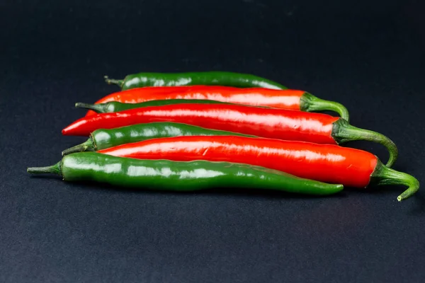 黑色背景上的绿色和红色辣椒。热辣食品. — 图库照片