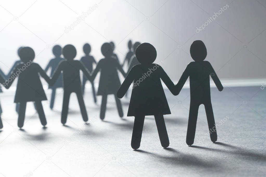 Black paper figure of a couple in front of a crowd of paper people holding hands on white surface. Social movement, leadership, protest concept.