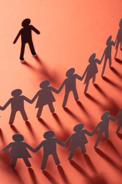 Kağıt insan figürü ayakta kırmızı yüzey üzerinde el ele tutuşarak kağıt insanların önünde. Bulling, segregasyon, çatışma kavramı.