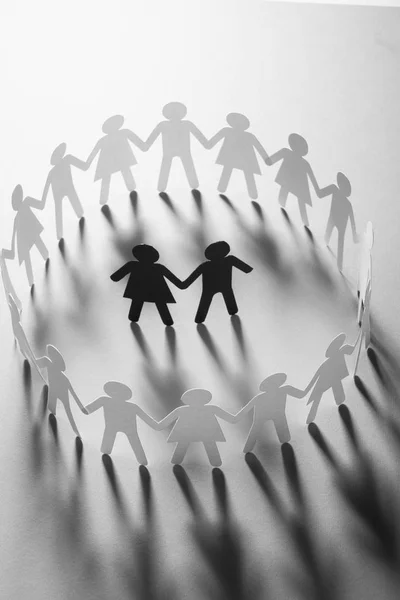 Paper figure of a couple surrounded by circle of paper people holding hands on white surface. Bulling, minorities, conflict concept. — Stock Photo, Image