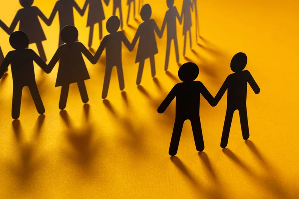 Figura de papel negro de pareja masculina frente a una multitud de personas de papel que se toman de la mano en la superficie naranja. Movimiento social, minorías, concepto de protesta . — Foto de Stock