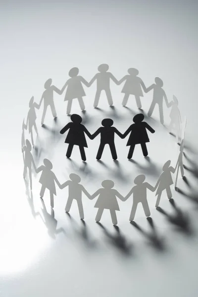 Tres figuras de papel humano rodeadas por un círculo de personas de papel cogidas de la mano en la superficie blanca. Bulling, segregación, concepto de conflicto . —  Fotos de Stock